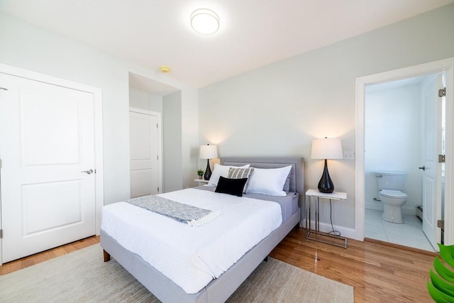 bedroom with ensuite bath, wood finished floors, and baseboards