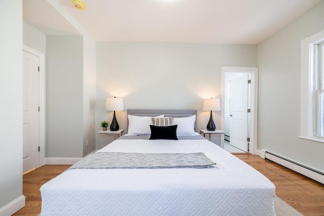 bedroom with a baseboard heating unit, baseboards, and light wood finished floors