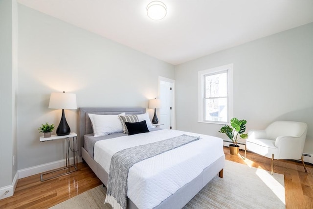 bedroom with a baseboard heating unit, wood finished floors, and baseboards