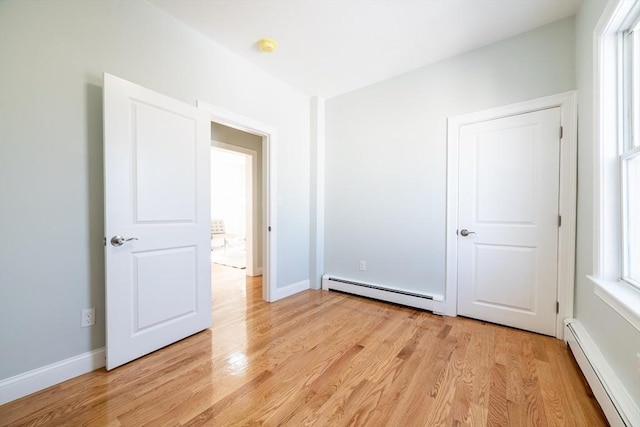 unfurnished bedroom featuring light wood-style floors, a baseboard radiator, a baseboard heating unit, and baseboards