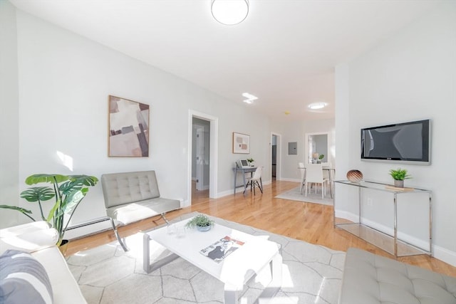 living area with a baseboard heating unit, light wood-type flooring, and baseboards