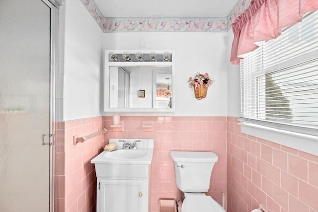 bathroom with vanity, toilet, tile walls, and a shower with shower door