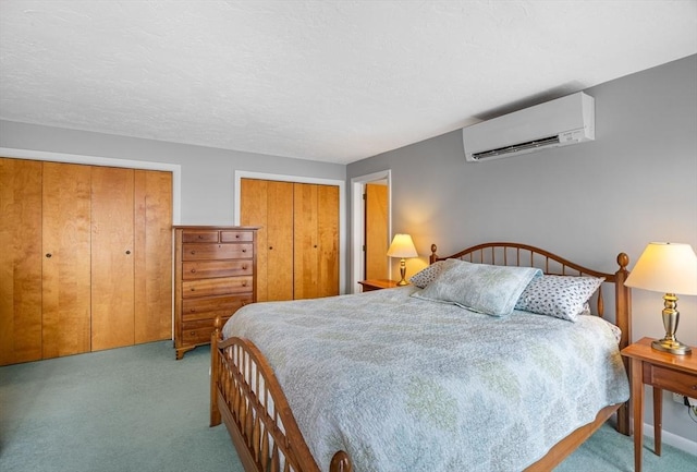 bedroom with two closets, carpet, a wall mounted air conditioner, and a textured ceiling