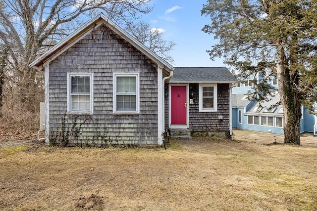 view of front of house featuring entry steps, a front lawn, and roof with shingles