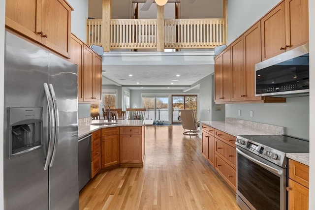 kitchen featuring appliances with stainless steel finishes, a peninsula, a towering ceiling, light wood-style floors, and a sink