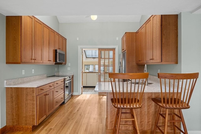 kitchen with appliances with stainless steel finishes, a breakfast bar area, light countertops, and a peninsula