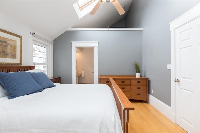 bedroom with ceiling fan, ensuite bath, vaulted ceiling with skylight, and wood finished floors