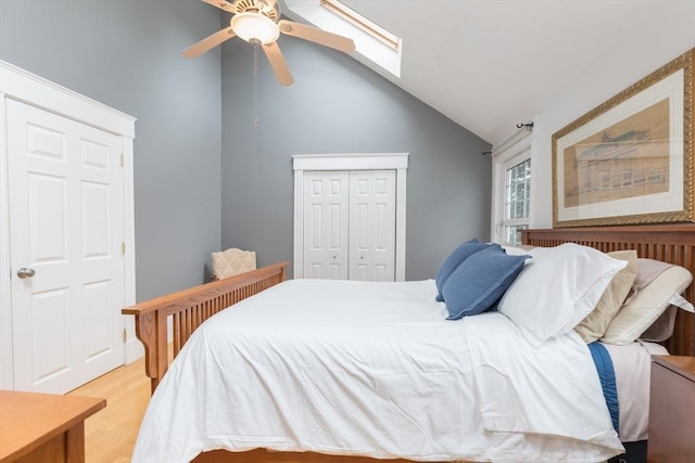 bedroom with light wood-style floors, lofted ceiling with skylight, a closet, and ceiling fan