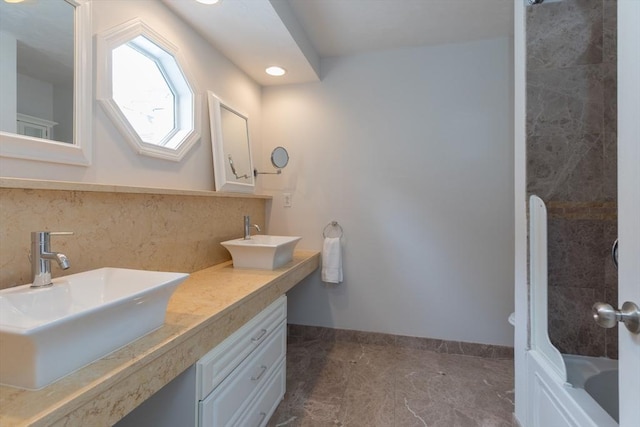 bathroom featuring baseboards, a sink, double vanity, and tasteful backsplash