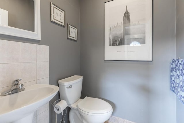 half bathroom with decorative backsplash, toilet, and a sink