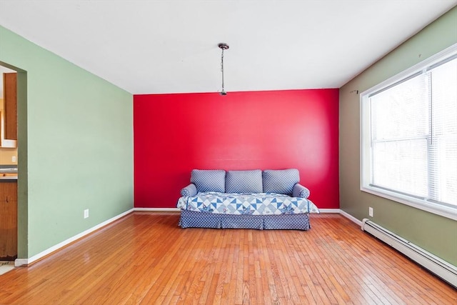 living area with a baseboard heating unit, baseboards, an accent wall, and hardwood / wood-style flooring