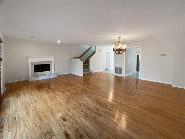 unfurnished living room with visible vents, a notable chandelier, a fireplace with raised hearth, wood finished floors, and stairs