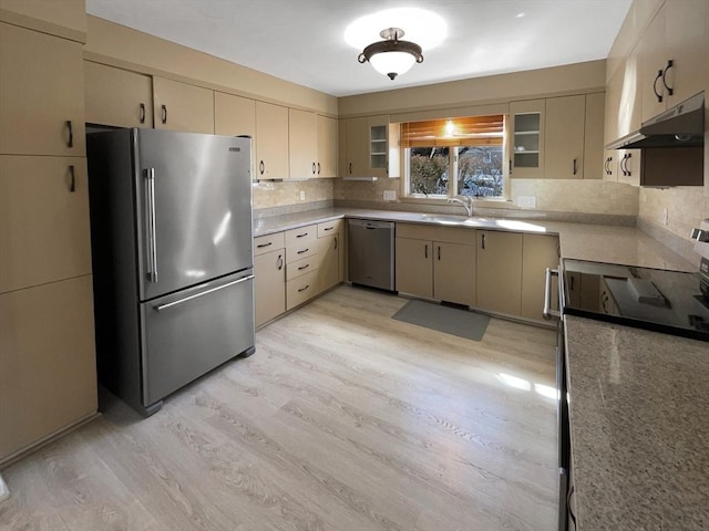 kitchen with cream cabinetry, under cabinet range hood, stainless steel appliances, light wood finished floors, and decorative backsplash