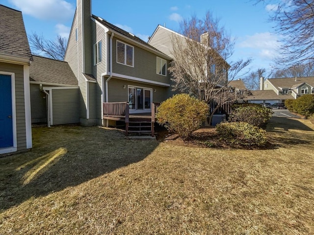 rear view of house with a yard, a deck, a chimney, and a shingled roof