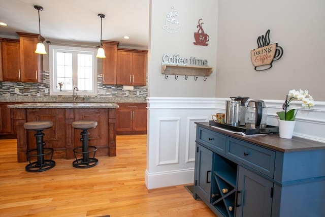 bar with wainscoting, backsplash, hanging light fixtures, light wood-style floors, and a sink