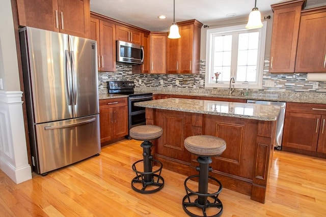 kitchen featuring a center island, light wood finished floors, decorative backsplash, appliances with stainless steel finishes, and a sink