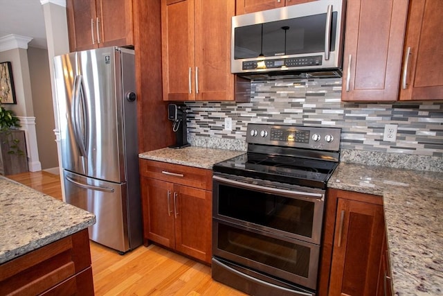 kitchen with stainless steel appliances, light wood-style floors, backsplash, and light stone counters