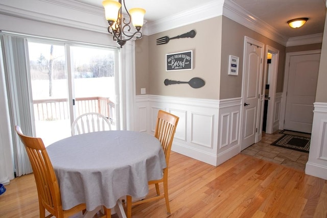 dining area with light wood-type flooring, wainscoting, an inviting chandelier, and crown molding