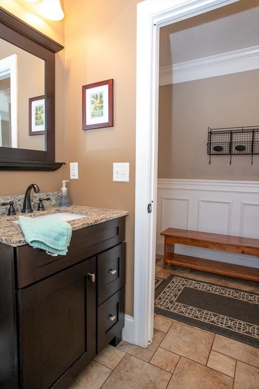 bathroom featuring wainscoting, crown molding, vanity, and a decorative wall