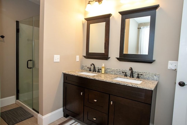 bathroom featuring double vanity, a shower stall, baseboards, and a sink