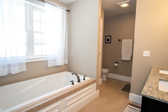 full bathroom with double vanity, toilet, wood finished floors, a jetted tub, and baseboards