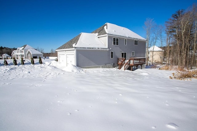 snow covered rear of property with a garage and a wooden deck