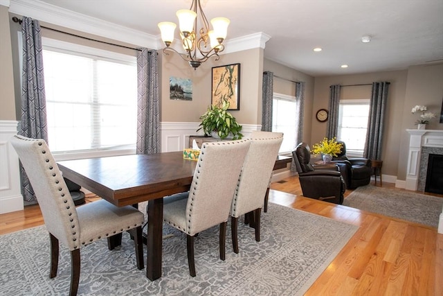 dining area featuring light wood finished floors, a wainscoted wall, crown molding, a decorative wall, and a high end fireplace