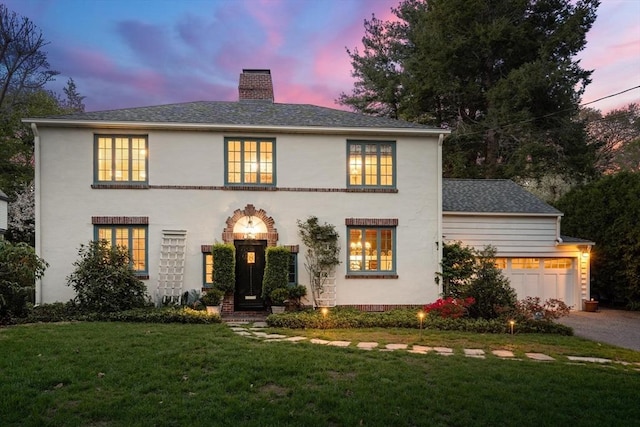 view of front of house with a chimney, aphalt driveway, an attached garage, a front lawn, and stucco siding