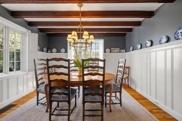 dining space featuring an inviting chandelier, beamed ceiling, light wood-style flooring, and a wealth of natural light
