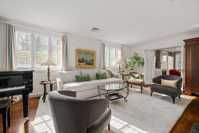living area featuring visible vents, baseboards, crown molding, and wood finished floors