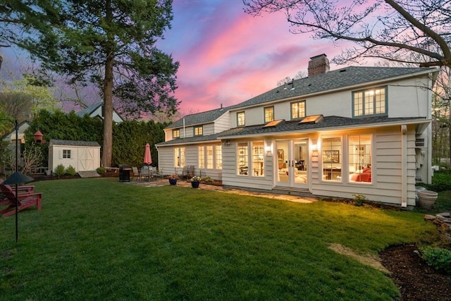 back of property featuring a chimney, french doors, a storage shed, an outdoor structure, and a yard