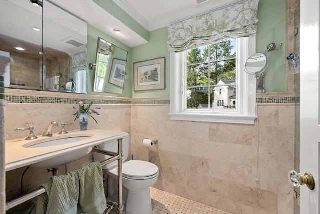full bath with crown molding, tile walls, a sink, toilet, and tiled shower