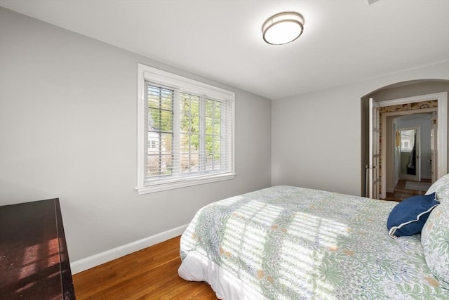 bedroom featuring baseboards, arched walkways, and wood finished floors