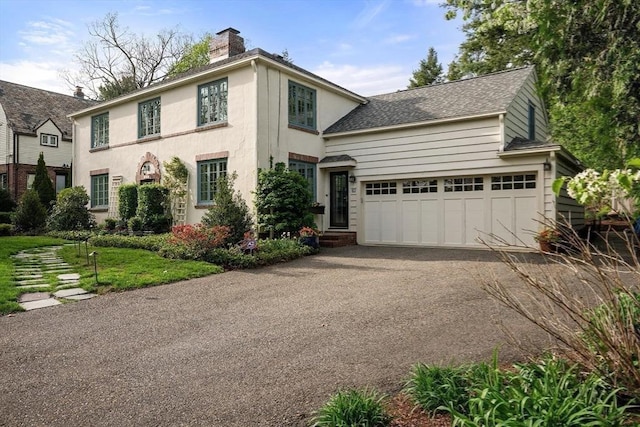 colonial house with driveway, a chimney, a garage, a shingled roof, and stucco siding