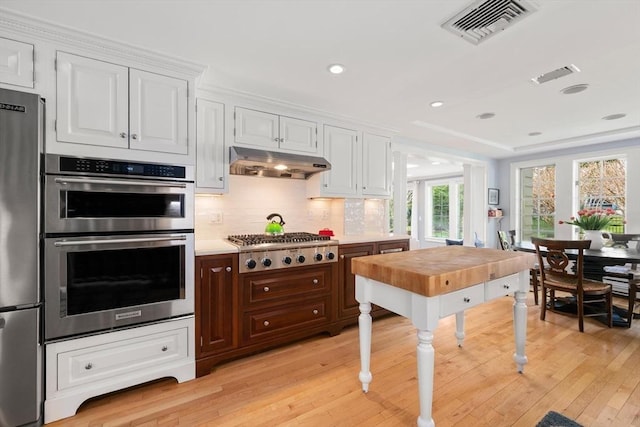 kitchen featuring appliances with stainless steel finishes, light countertops, light wood-type flooring, under cabinet range hood, and visible vents