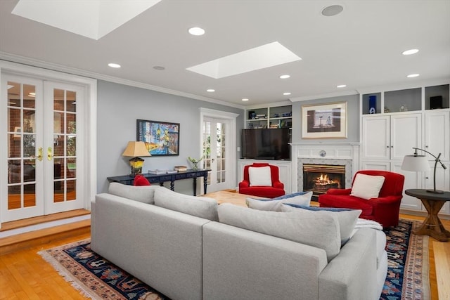 living room with crown molding, wood finished floors, a skylight, french doors, and a premium fireplace