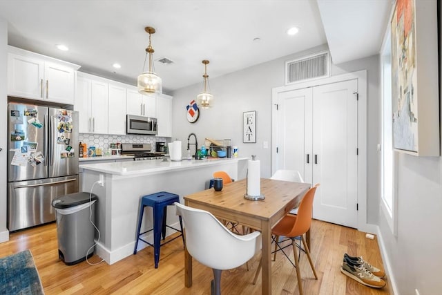 kitchen with appliances with stainless steel finishes, tasteful backsplash, light wood-style flooring, light countertops, and white cabinetry