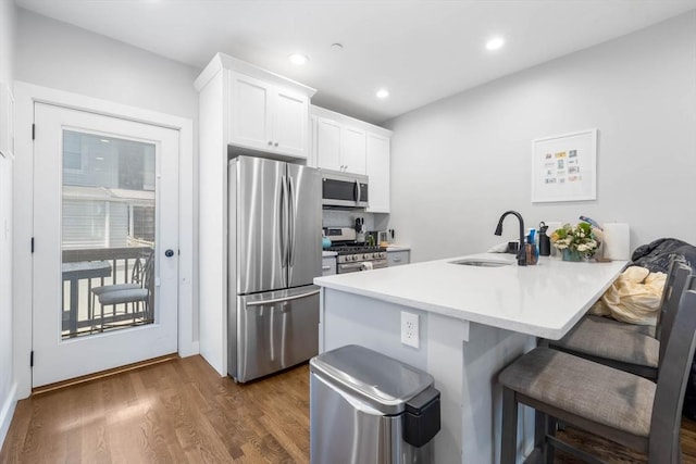 kitchen featuring appliances with stainless steel finishes, a sink, a kitchen bar, white cabinetry, and dark wood finished floors