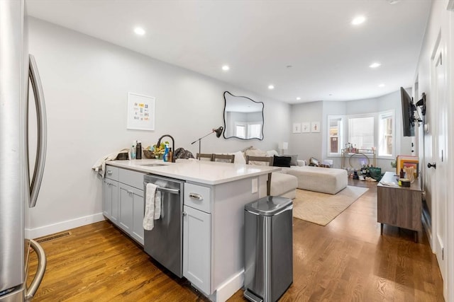 kitchen featuring appliances with stainless steel finishes, a sink, a peninsula, open floor plan, and wood finished floors