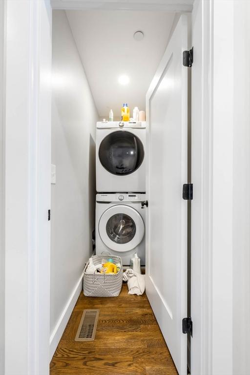 clothes washing area featuring stacked washer / drying machine and wood finished floors