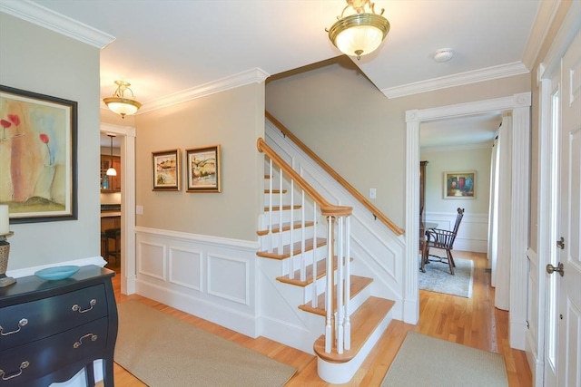 staircase with a wainscoted wall, crown molding, a decorative wall, and wood finished floors