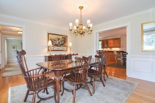 dining space with light wood finished floors, an inviting chandelier, crown molding, and wainscoting