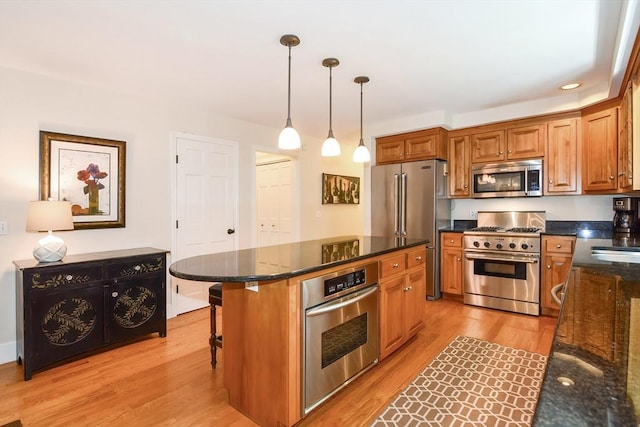 kitchen with high quality appliances, hanging light fixtures, light wood-type flooring, brown cabinets, and dark stone countertops