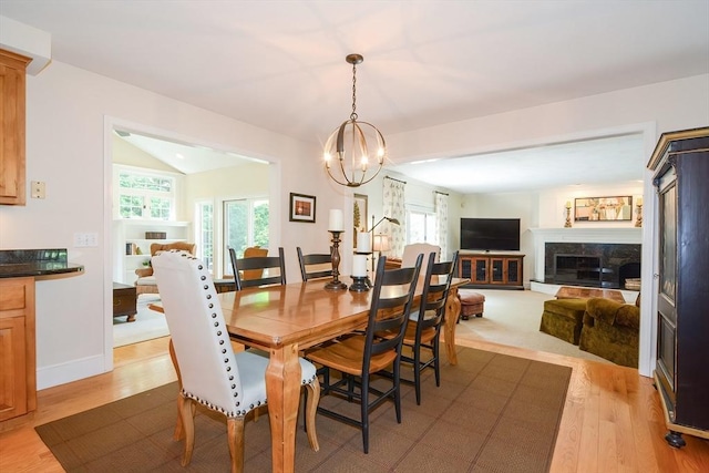 dining room with light wood-style floors, vaulted ceiling, a wealth of natural light, and a high end fireplace