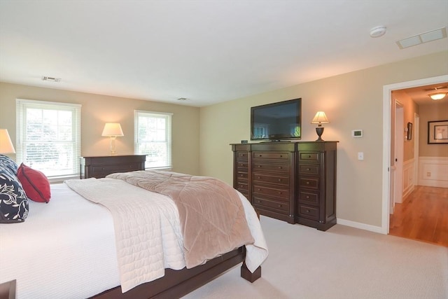 bedroom with a wainscoted wall, baseboards, visible vents, and light colored carpet