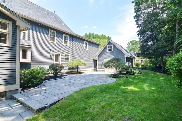 rear view of property with a patio, a shingled roof, and a lawn