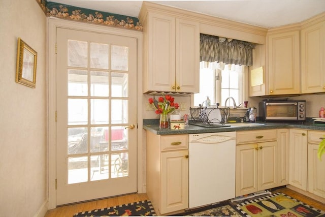 kitchen with white dishwasher, sink, cream cabinets, and light wood-type flooring