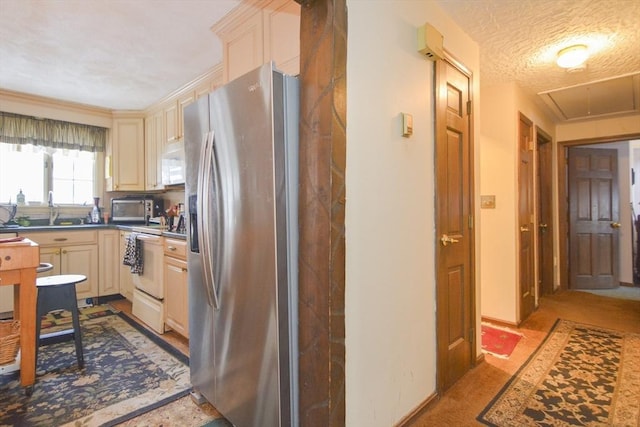 kitchen featuring sink, white appliances, cream cabinets, and a textured ceiling