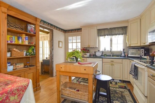 kitchen with cream cabinets, sink, white appliances, and light hardwood / wood-style floors