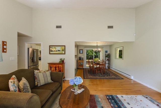 living room with baseboard heating, wood-type flooring, a chandelier, and a high ceiling